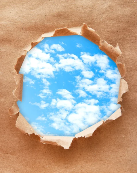 Fond bleu ciel avec des nuages à travers un trou dans du papier artisanal — Photo
