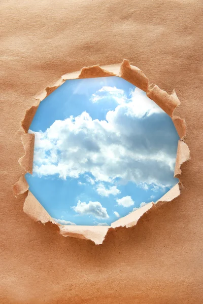 Fond bleu ciel avec des nuages à travers un trou dans du papier artisanal — Photo