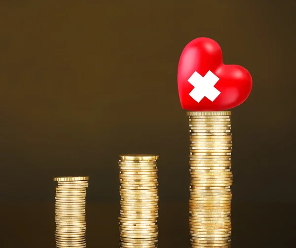 Red heart with cross sign on stack of coins on brown background — Stock Photo, Image