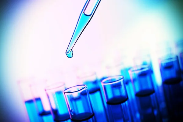 Pipette adding fluid to the one of test-tubes on bright background — Stock Photo, Image