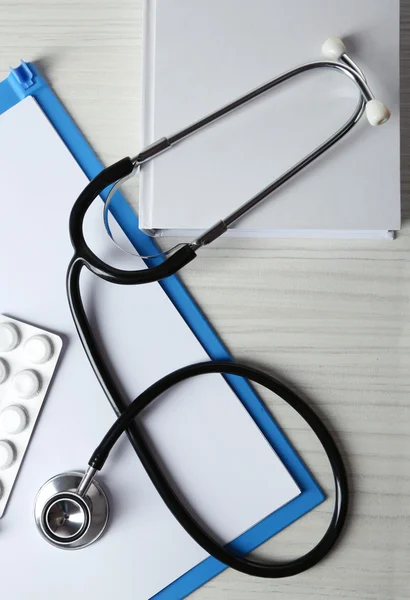 Estetoscopio médico con libro y carpeta en mesa de madera —  Fotos de Stock