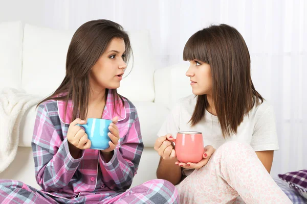 Beautiful girls twins in pajamas drinking tea at home — Stock Photo, Image