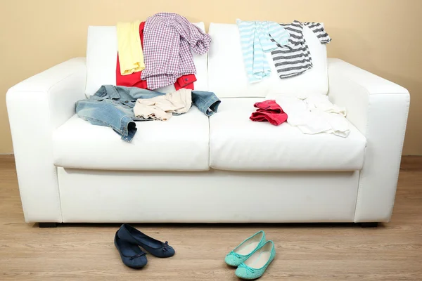 Abbigliamento colorato su divano bianco e scarpe femminili su sfondo parete chiara — Foto Stock