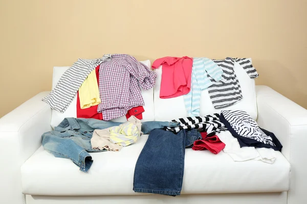 Messy clothing on white sofa, on light wall background — Stock Photo, Image