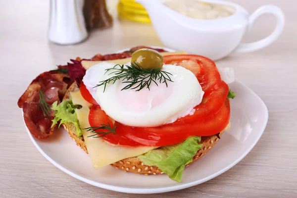 Sandwich with poached egg, tomato and bacon on plate on wooden background — Stock Photo, Image