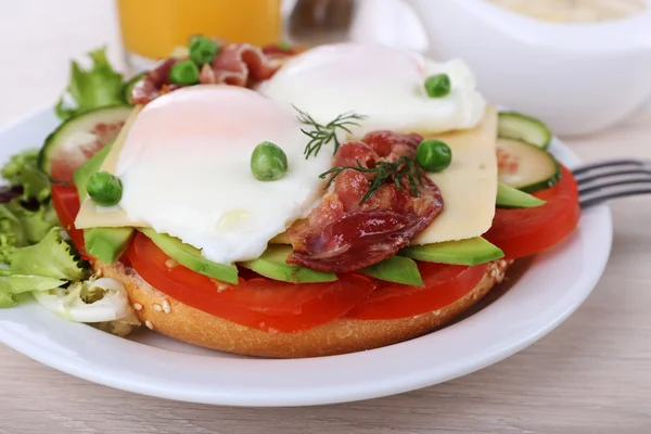 Sandwich with poached eggs, bacon and vegetables on plate on wooden background — Stock Photo, Image
