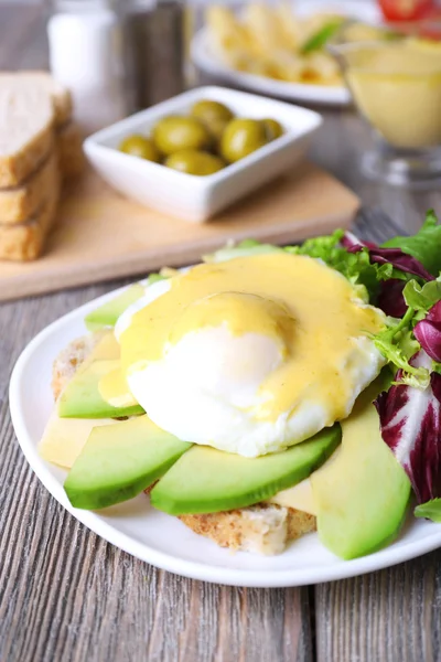 Toast with egg Benedict and avocado on plate on wooden table — Stock Photo, Image