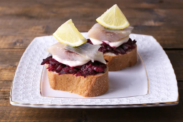 Rye toasts with herring and beets on plate on wooden background — Stock Photo, Image