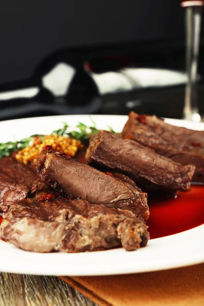 Bife com molho de vinho no prato e garrafa de vinho no fundo escuro — Fotografia de Stock