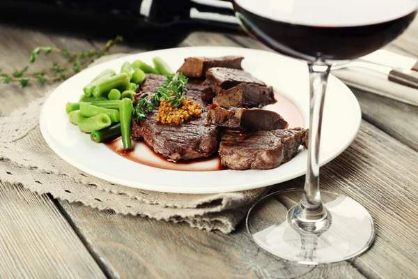 Filete en plato con botella de vino sobre fondo de madera —  Fotos de Stock