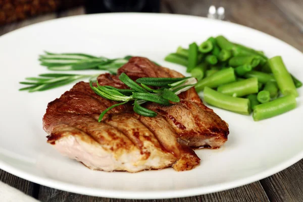 Steak with herbs on plate on wooden table — Stock Photo, Image