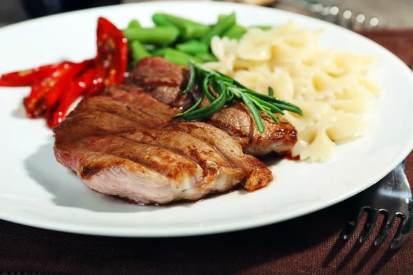 Steak aux légumes et pâtes sur assiette en bois — Photo