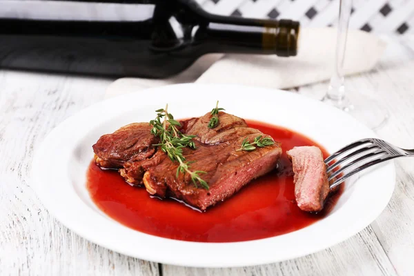 Steak with wine sauce on plate with bottle of wine on wooden background — Stock Photo, Image