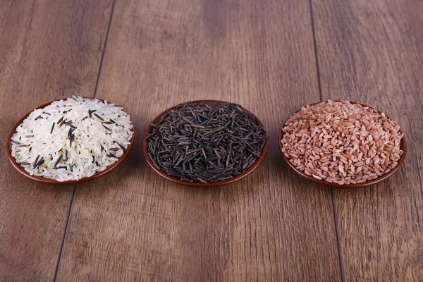 Different kinds of rice on plates on wooden background — Stock Photo, Image