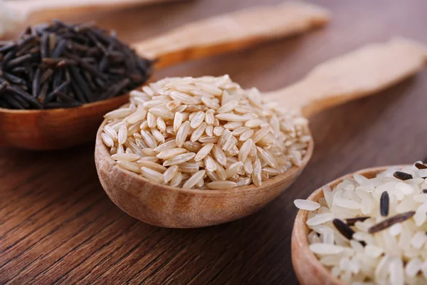 Diferentes tipos de arroz em colheres no fundo de madeira — Fotografia de Stock