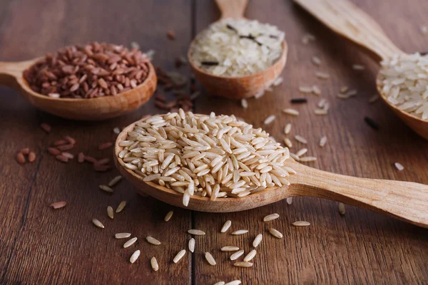 Diferentes tipos de arroz en cucharas sobre fondo de madera — Foto de Stock