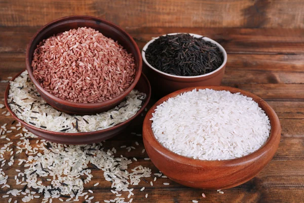 Diferentes tipos de arroz em tigelas em fundo de madeira — Fotografia de Stock