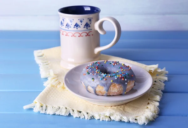 Glazed donut with cup of milk on napkin and color wooden planks background — Stock Photo, Image