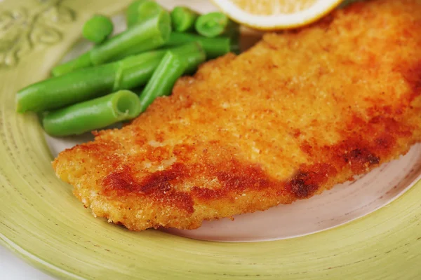 Filetto di pesce fritto impanato e patate con asparagi e limone affettato su fondo piatto verde — Foto Stock