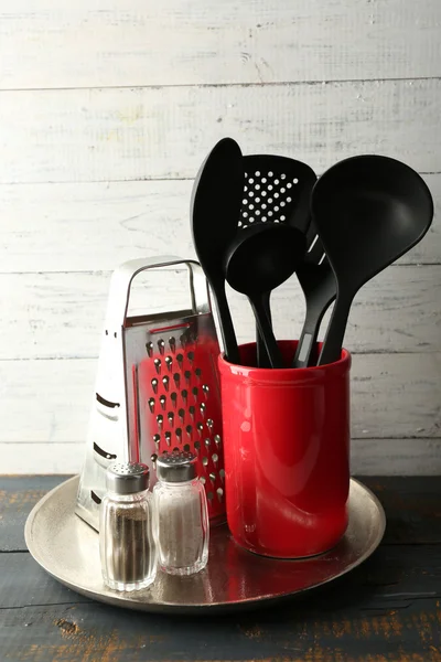 Plastic kitchen utensils in red cup on wooden background — Stock Photo, Image