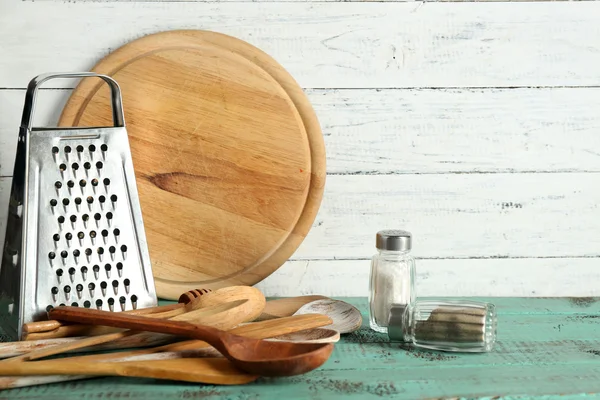 Деревянная посуда с металлической теркой и доской для резки на фоне цветного стола и досок — стоковое фото