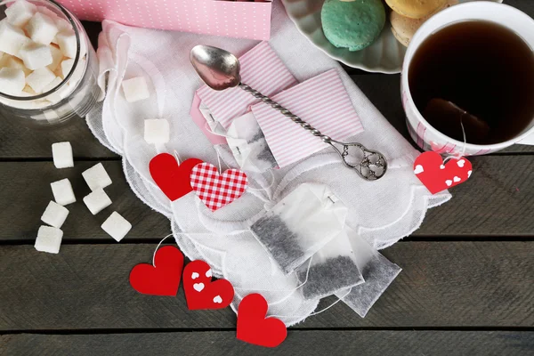 Etiquetas de la bolsa de té en forma de corazón, macarrones y taza de té sobre fondo de madera — Foto de Stock