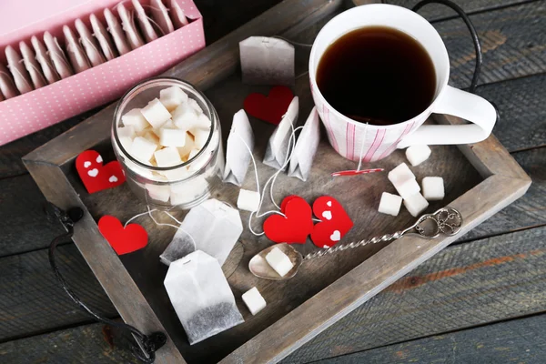 Heart shaped teabag tags, box and cup of tea on wooden background — Stock Photo, Image