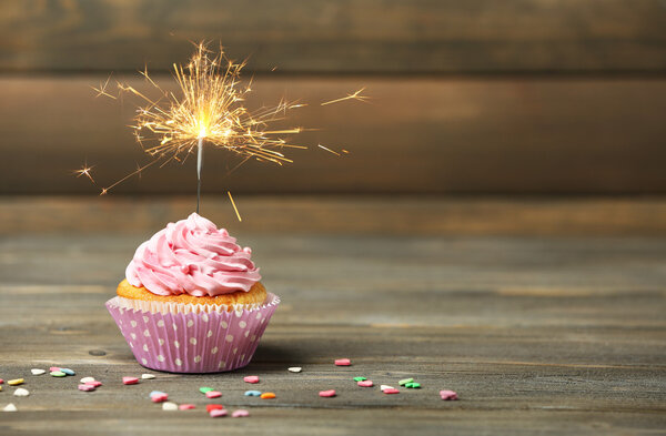 Cupcake con bengala en la mesa sobre fondo de madera — Imagen de stock Cupcake con bengala en la mesa sobre fondo de madera Fotos De Stock