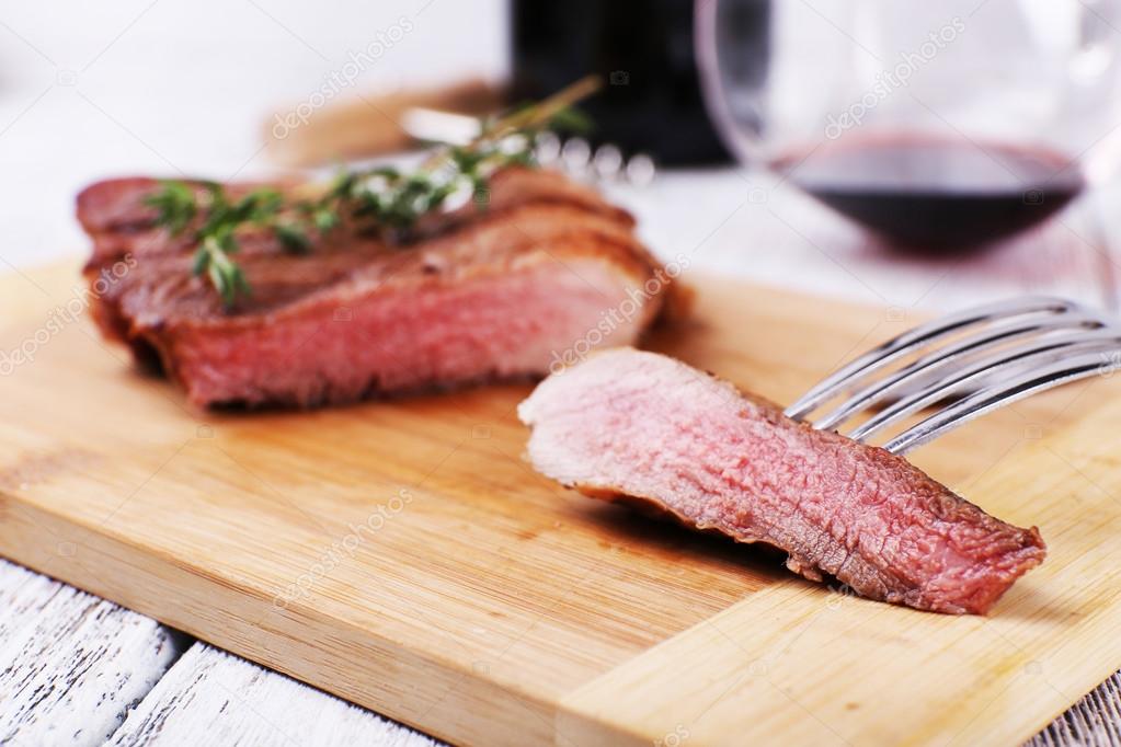 Steak with herbs on wooden stand and wine on table close up