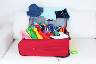 Bavul giyim ve çocuk oyuncak beyaz kanepe ve tuğla duvar arka planda dolu