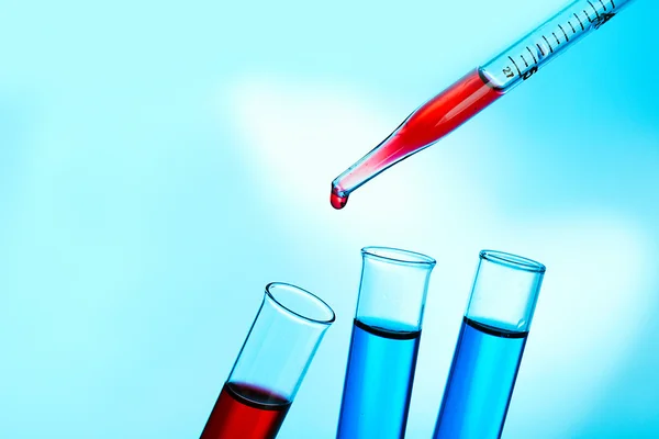 Pipette adding fluid to the one of test-tubes on blue background — Stock Photo, Image