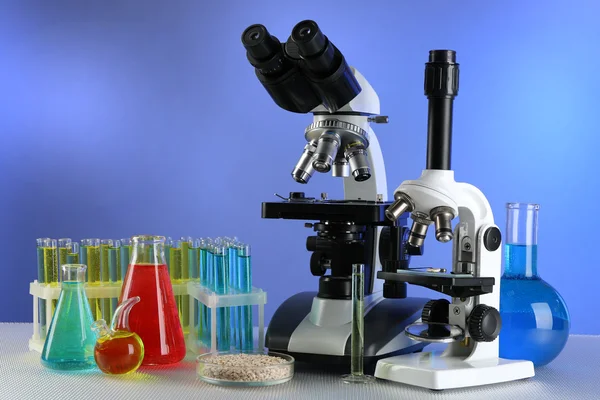 Microscopios, placa Petri con muestras de grano y tubos de ensayo sobre la mesa, sobre fondo de color —  Fotos de Stock