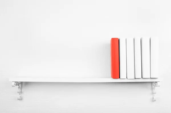 Libros en blanco con uno rojo en la estantería sobre fondo blanco de la pared —  Fotos de Stock