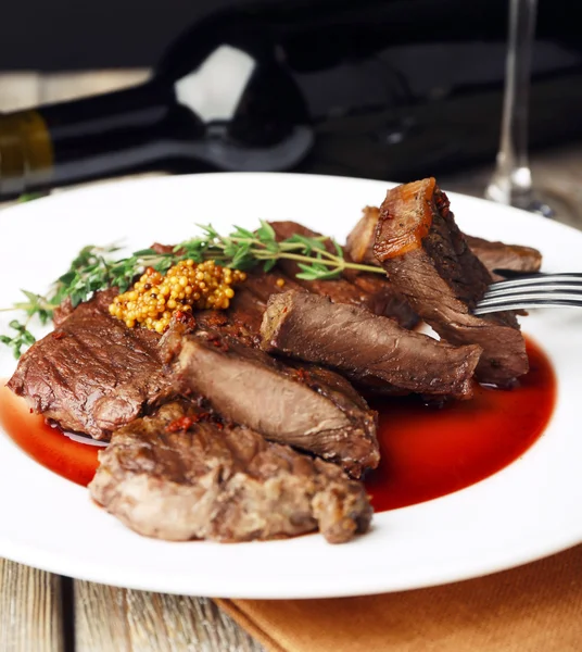 Bife com molho de vinho no prato e garrafa de vinho no fundo escuro — Fotografia de Stock