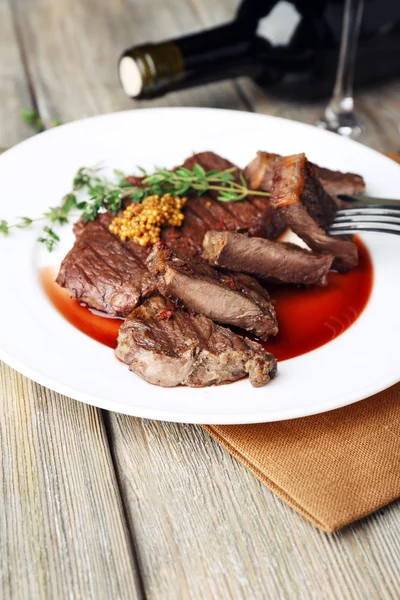 Steak on plate with bottle of wine on wooden background — Stock Photo, Image