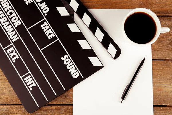 Movie clapper with paper, pen and cup of coffee on wooden planks background — Stock Photo, Image