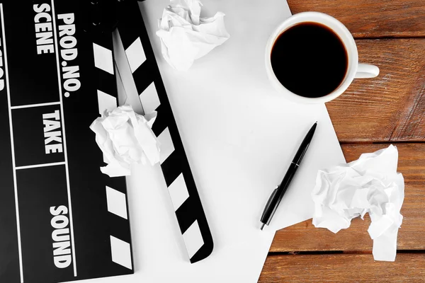 Movie clapper avec du papier, stylo et tasse de café sur des planches de bois fond — Photo