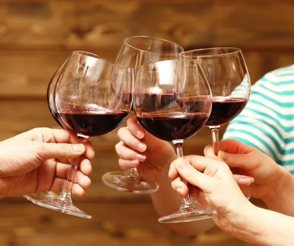 Clinking glasses of red wine in hands on rustic wooden planks background — Stock Photo, Image