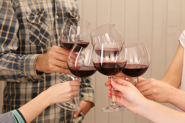 Звон бокалов красного вина в руках на фоне цветных деревянных досок — стоковое фото
