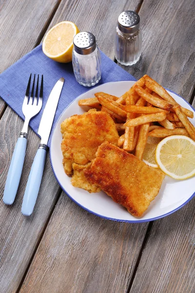 Filetes de peixe frito empanado e batatas com limão fatiado e talheres no prato e pranchas de madeira fundo — Fotografia de Stock