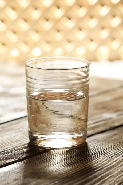 Glass of clean mineral water on wooden surface and lattice background — Stock Photo, Image