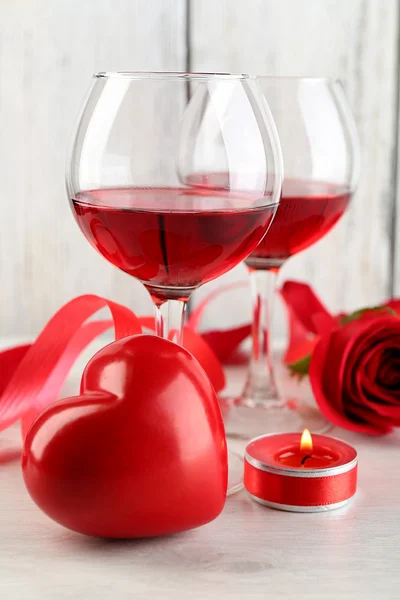 Složení s červeným vínem ve skleněných, červené růže a dekorativní srdce na barevné dřevěné pozadí — Stock fotografie