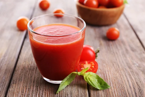 Tomatjuice i glass med basilikum og tomater og kirsebær av tre på bakgrunn av planker – stockfoto