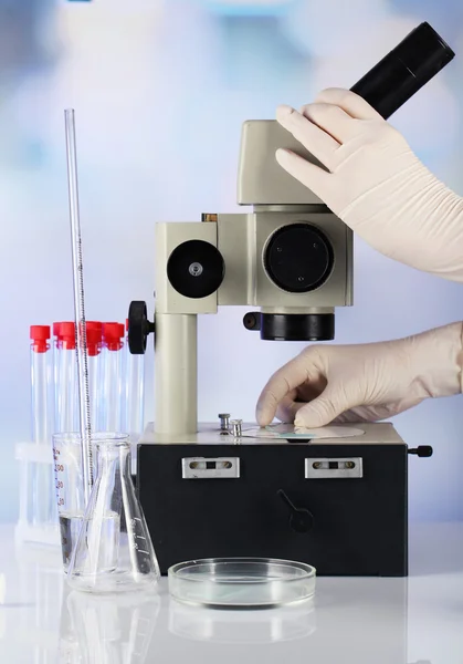Ruce pomocníka v rukavicích, práce s mikroskopem poblíž zkumavky na rozmazané pozadí — Stock fotografie