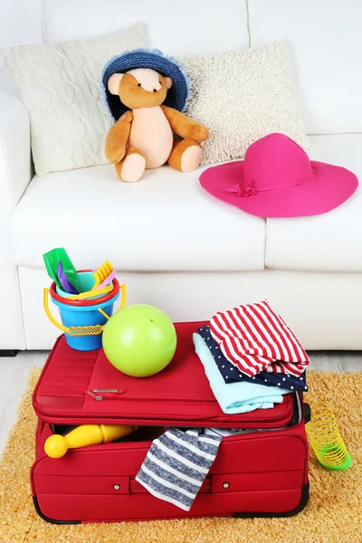 Suitcase packed with clothes and child toys on fur rug and white sofa background — Stock Photo, Image