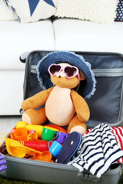 Βαλίτσα γεμάτη με ρούχα και παιδί παιχνίδια στην κουβέρτα γουνών και φόντο λευκό καναπέ — Φωτογραφία Αρχείου