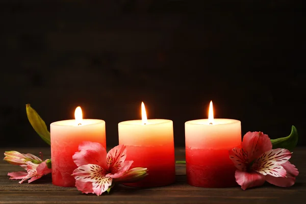 Vackert ljus med blommor på träbord, på mörk bakgrund — Stockfoto