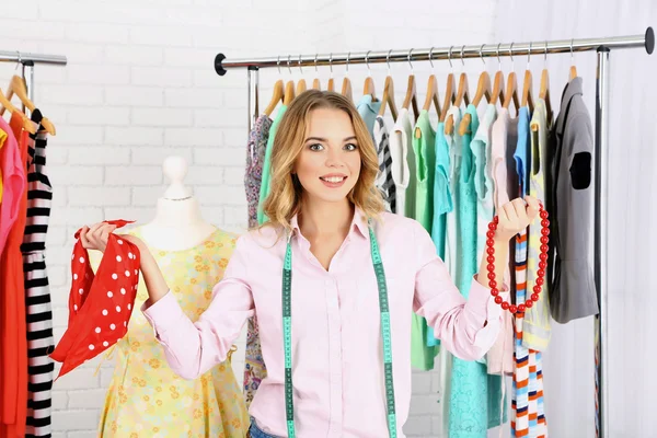 Schöne junge Stylistin in der Nähe von Gestell mit Kleiderbügeln — Stockfoto