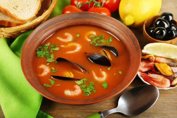 Tasty soup with shrimps, mussels, tomatoes and black olives in bowl on wooden background — Stock Photo, Image