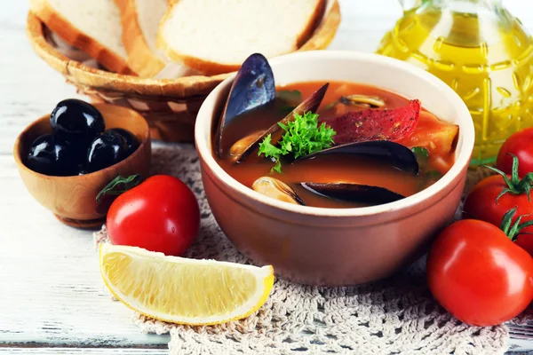 Tasty soup with shrimps, mussels, tomatoes and black olives in bowl on wooden background — Stock Photo, Image